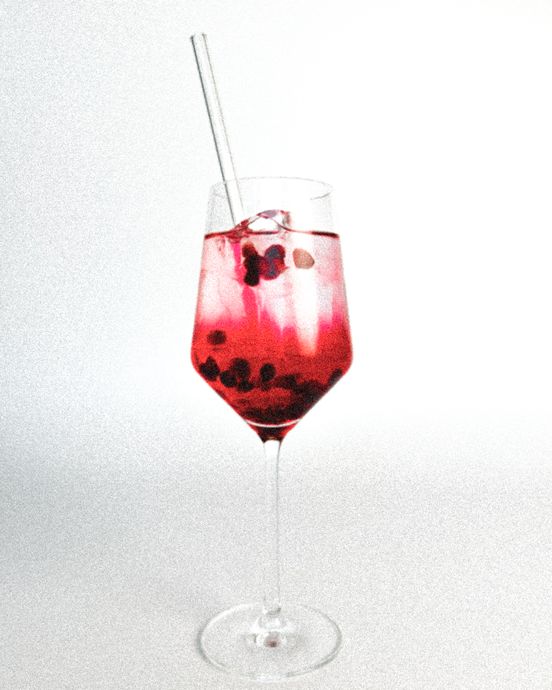 Ein Weinglas mit einem GRANADA NIGHTS Spritz, Eirwürfel, Granatapfelkernen und Strohhalm.