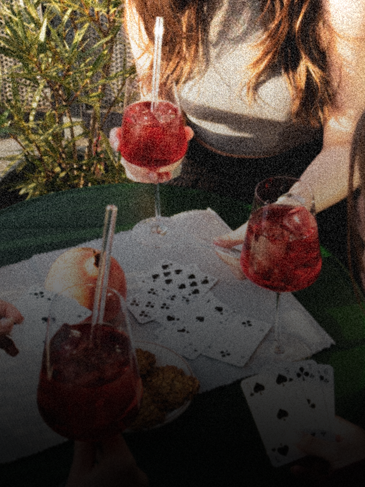 Drei Personen die Karten spielen und GRANADA NIGHTS Spritz trinken. Auf dem Tisch liegt außerdem noch ein Granatapfel und ein Teller mit Snacks.