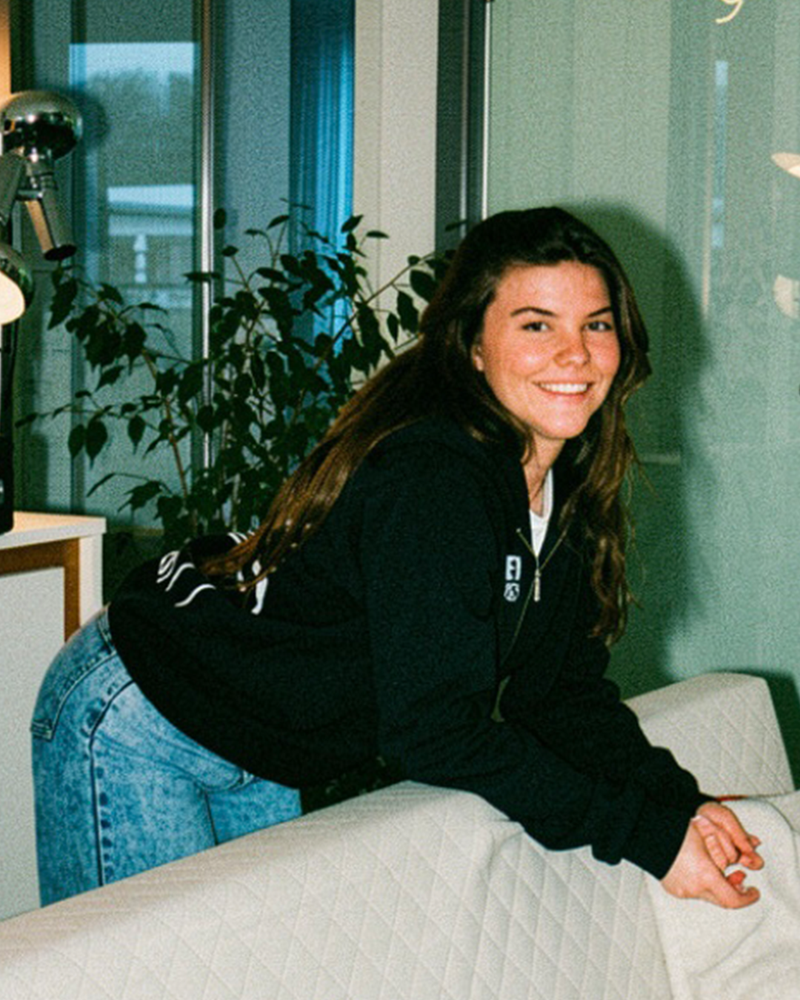 Eine Frau die sich über ein Sofa lehnt mit einer HEYBEVS Jacke.